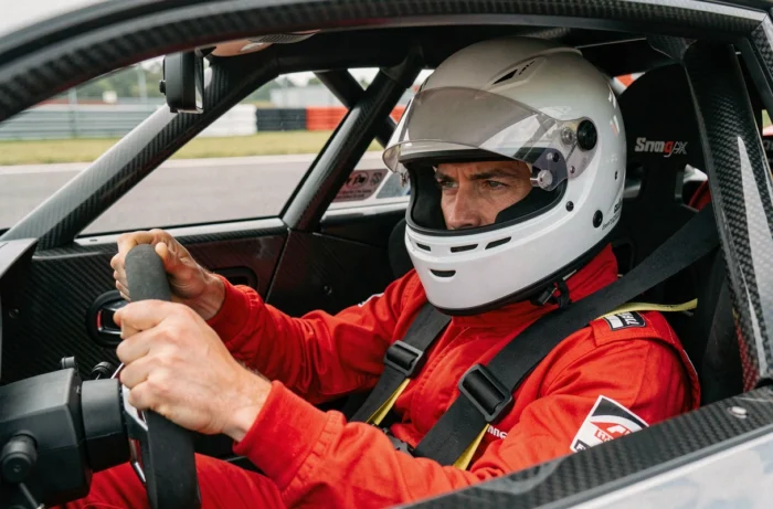 Pilote en combinaison rouge concentré au volant d'un bolide de stage de pilotage sur circuit automobile